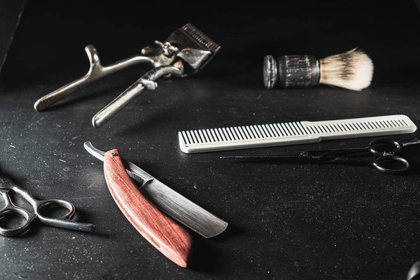 Vintage-Friseurausrüstung auf schwarzem Hintergrund. professionelle Friseurwerkzeuge. Schere, Handhaarschneider, Rasiermesser, Rasierpinsel, Kamm - Foto, Bild