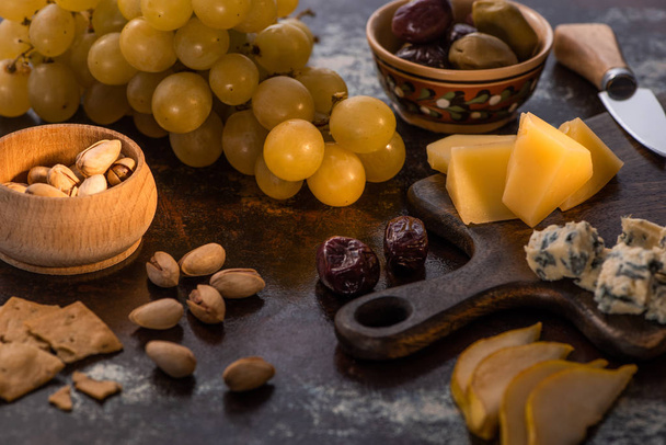 cheese platter with olives, fruits, crackers and pistachios near knife - Photo, Image