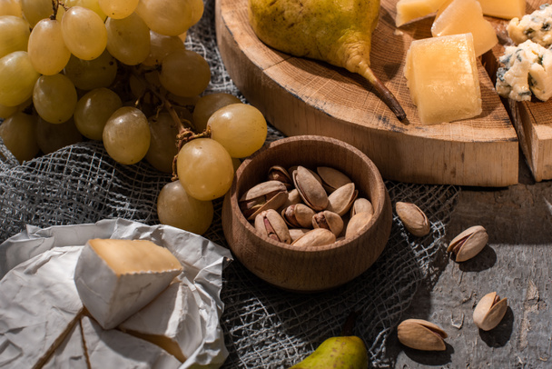 Fromage avec poire sur planche de bois à côté de raisins, pistaches et camembert sur fond gris
 - Photo, image