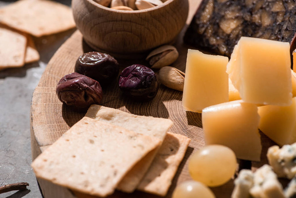 Enfoque selectivo de galletas saladas, aceitunas, uvas, pistachos y trozos de queso sobre fondo de madera
 - Foto, Imagen