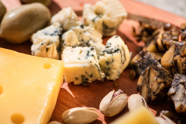 Selective focus of pieces of cheese, pistachios and olive on wooden background - Foto, immagini