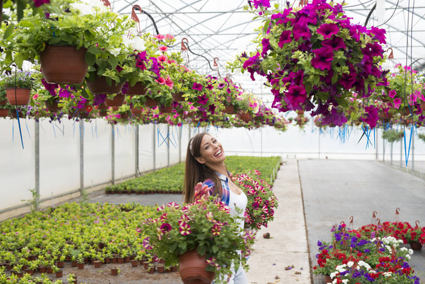 Happy smiling florist arranging flowers and enjoying work at greenhouse garden. - Photo, Image