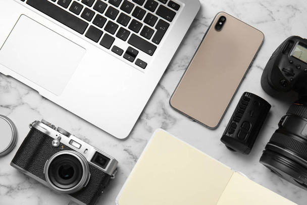 Flat lay composition with laptop, cameras and smartphone on white marble table. Designer's workplace - Фото, изображение
