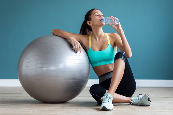 Sporty young woman drinking water while doing exercise with the ball on the gym. - Photo, Image