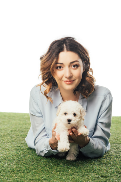 smiling woman holding Havanese puppy and lying on grass isolated on white - Zdjęcie, obraz