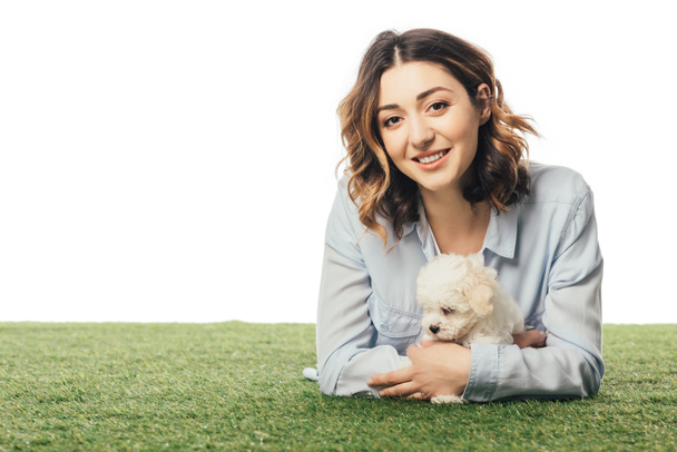 smiling woman holding Havanese puppy and lying on grass isolated on white - Photo, Image