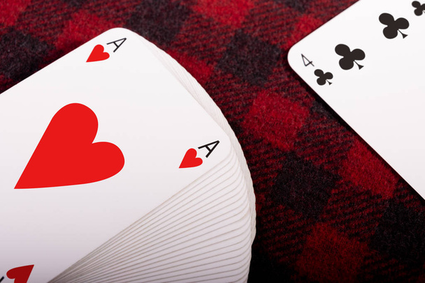 Full deck of playing cards with ace of hearts on top and card club 4 lying on checkered plaid. Horizontal photo. Place for text - Photo, Image