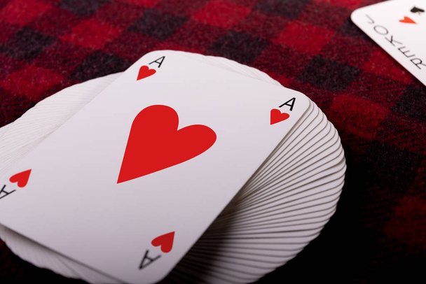Plný balíček hracích karet se srdcovým esem na vrchu a žolíkem ležícím na kostkovaném kostkovaném kostýmu. Vodorovná fotka. Místo pro text - Fotografie, Obrázek
