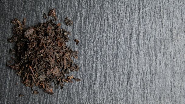 Pile of scattered black tea on a stone plate with copy space. - Photo, Image
