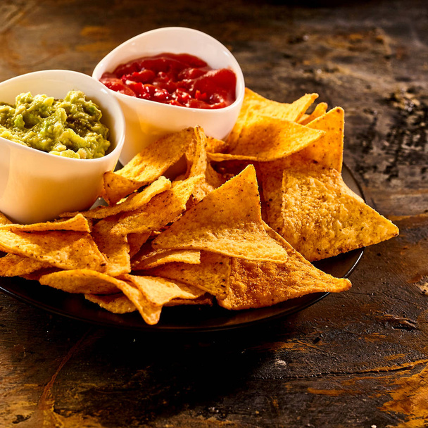 Plate full of guacamole, salsa and nacho chips close up on old worn out dark stained table - Фото, зображення