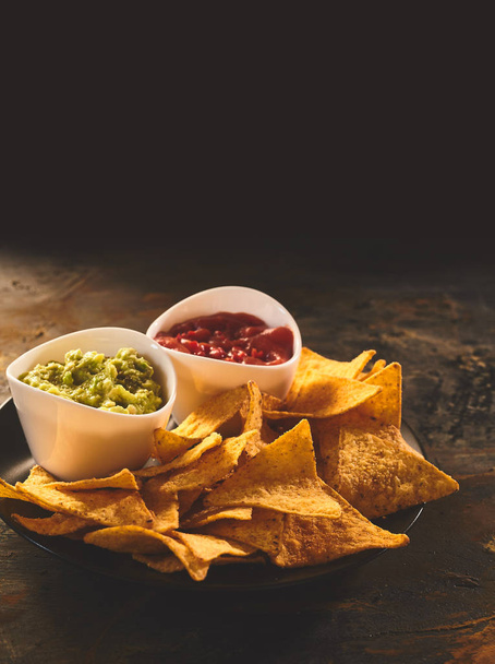 Plate of Mexican cuisine appetizer of triangular yellow corn tortilla chips beside little bowls of guacamole and salsa dip - Foto, afbeelding