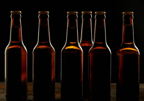 Branding and marketing concept for beer with a line of unopened unlabelled full blank brown bottles on a dark shadowy background conceptual of Oktoberfest or nightlife - Foto, imagen