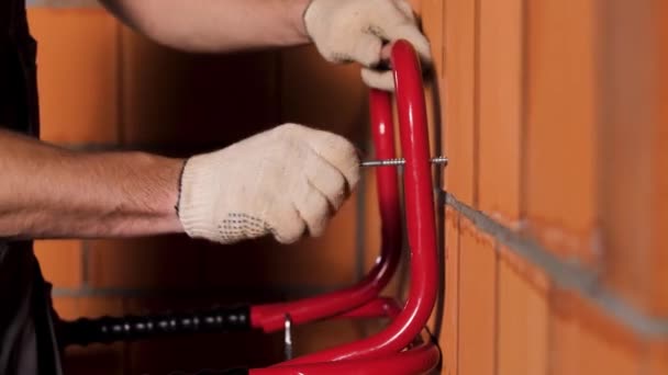 Side view of a man tightening the screw inside the red ceramic blocks. Stock footage. Worker during the process of attaching the metal detail to the wall. - Footage, Video