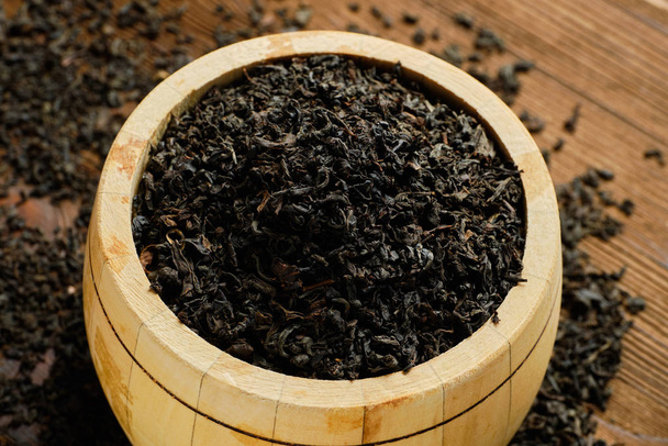 Black tea in barrel and scattered tea on wooden background. View from top. - Fotoğraf, Görsel
