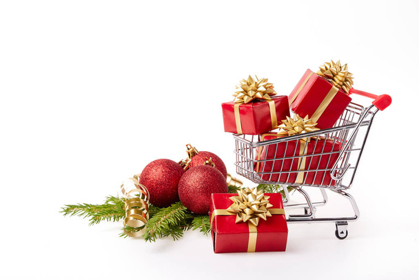 Shopping trolley with gift boxes and brenches of fir-tree with decoration on a white background. Christmas and New Year sale. - Фото, изображение