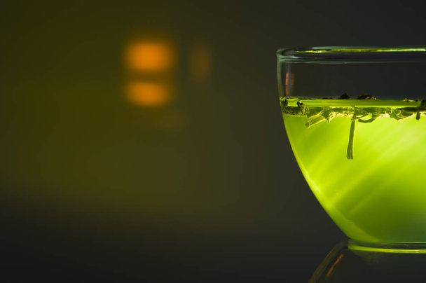 angled closeup of a glass cup in front of green illuminated background with bright reflex. - Photo, Image