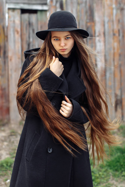 Young beautiful fashionable woman in black hat with long hair posing on woody background - Foto, Imagen