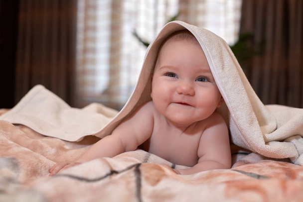 Sweet small baby with  towel lies on the bed at home. - Foto, imagen