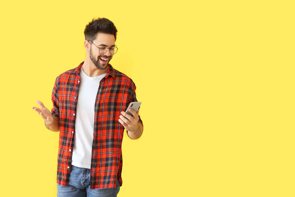 Happy young man with mobile phone on color background - Foto, afbeelding