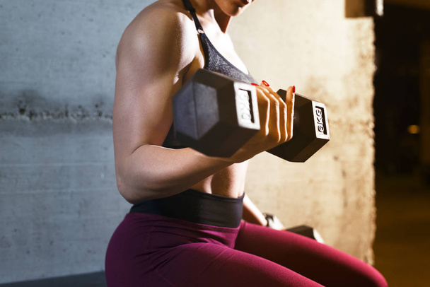 Close-up zicht van een sterke spieropbouw fitness vrouw tillen gewicht en training biceps in de sportschool. - Foto, afbeelding