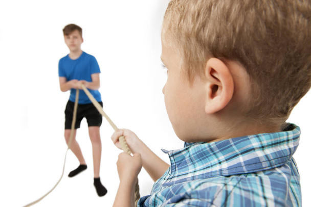 two brothers draw each isolated on white at the ends of a rope. younger brother (9 years) in sharp focus in the foreground with his back to the camera. older brother (13 years) blurred face in the background as a full body view of the camera. - Photo, Image