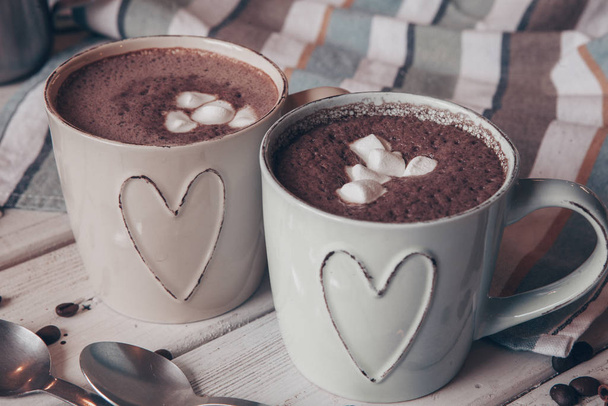 Two cups of hot cocoa with marshmallows and cinnamon sticks on wooden background. Love. Cocoa drink. Valentines day treat ideas. - 写真・画像