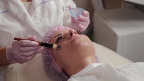 Професійний косметолог наносить маску на обличчя клієнта пензлем
. - Кадри, відео