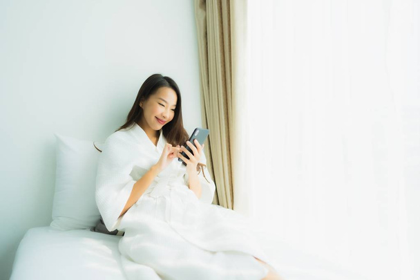 Молода азіатська жінка використовує мобільний смартфон на ліжку
 - Фото, зображення