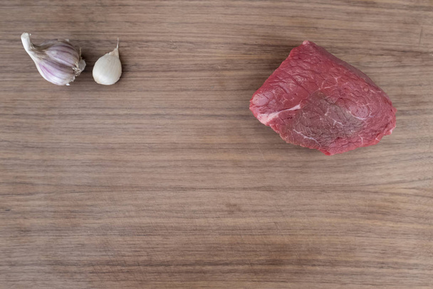 Koyu ahşap kesme tahtasına sarımsaklı çiğ biftek. - Fotoğraf, Görsel