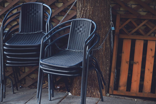 schwarze Café-Outdoor-Stühle gestapelt und an einen Baum gekettet - Foto, Bild
