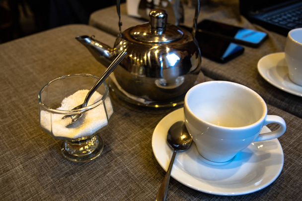 Metalli teekannu teetä panimo, valkoinen keraaminen kuppi, lasi maljakko sokeria pöydälle kahvilassa
. - Valokuva, kuva