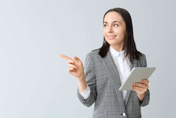 Young businesswoman with tablet computer showing something on grey background - Photo, Image