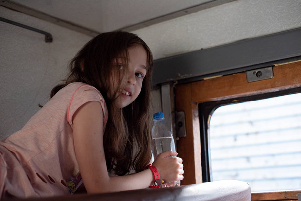 Mädchen in einer Fahrt in einem alten Zug. In der Nähe liegt eine Flasche Wasser. - Foto, Bild