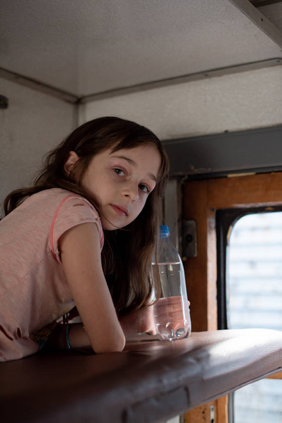 Mädchen in einer Fahrt in einem alten Zug. In der Nähe liegt eine Flasche Wasser. - Foto, Bild