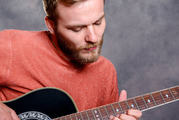 young bearded man in red shirt playing acoustic guitar - Valokuva, kuva