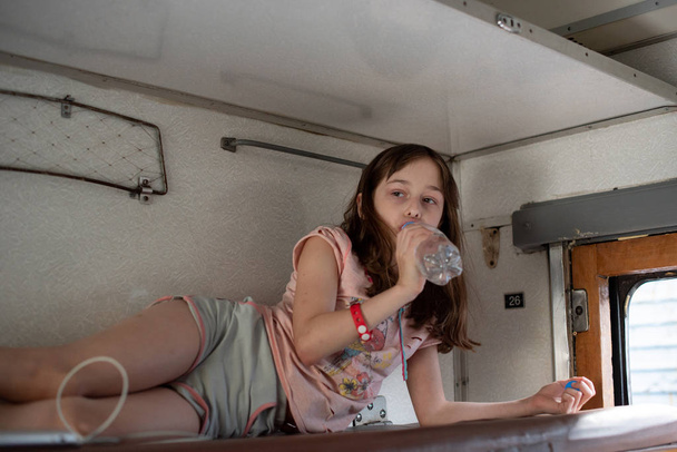 Dziewczyna na przejażdżce starym pociągiem. W pobliżu znajduje się butelka wody. - Zdjęcie, obraz