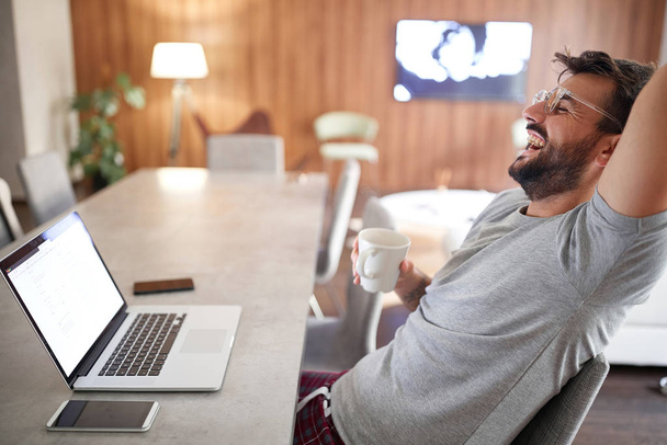 Glimlachende man drinken ochtend kopje koffie tijdens het werken op laptop. - Foto, afbeelding