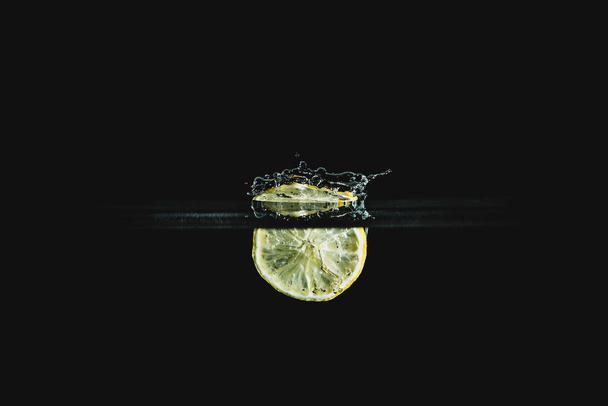 Part of fruit, fresh and delicious lemon isolated on dark, black background. Citrus falls in water and creating a splash. The concept of healthy eating, consuming fruit. - Photo, Image