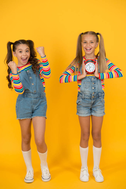 two happy girls hold alarm clock. back to school. summertime. discipline and time management. teenage girls yellow wall. children vintage clock. counting for lunch time. children break concept - Foto, Imagem