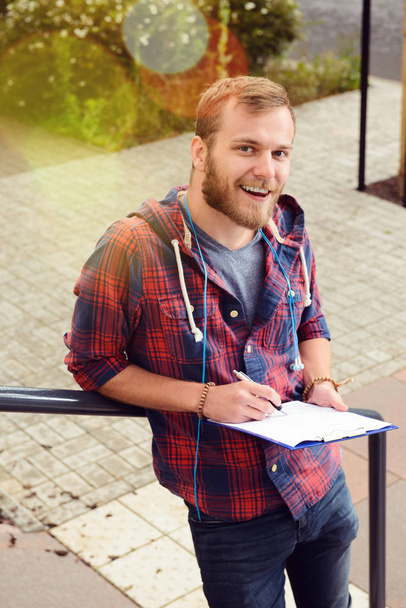 young man bearded standing by stairs with clipboard and writing - Foto, Bild