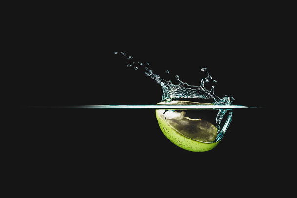 Part of fruit, Fresh and delicious green apple isolated against dark, black background. green apple dropping in water and creating a splash. The concept of healthy eating, consuming fruit. - Photo, image