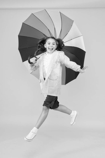 Rainy days bright accessories. Rain is not so bad if you have water resistant clothes. Simple happiness. I do not care. Carefree schoolgirl jumping with umbrella waterproof rain coat. Autumn rain - 写真・画像
