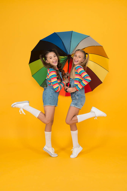 Any weather is good. children enjoy rainy autumn. fall kid fashion. feeling safe and comfortable. Good mood at any weather. small girl under colorful umbrella. two happy kids yellow background - Foto, Imagen