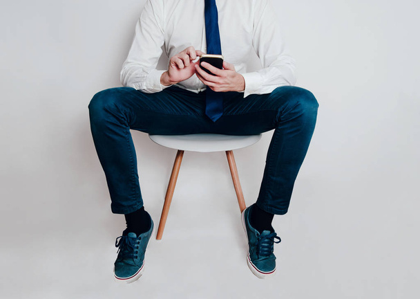 The man sits on a chair and uses a mobile phone. The man is waiting for a doctor's appointment. The man is waiting for a recruitment interview, he uses a smartphone. - Foto, Imagem