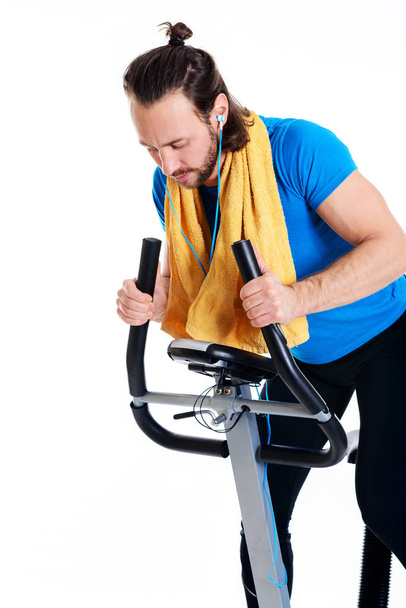 young man in blue shirt train with fitness machine and listening music - Photo, Image