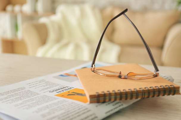 Gafas con estilo con periódico y cuaderno en la mesa en casa
 - Foto, Imagen