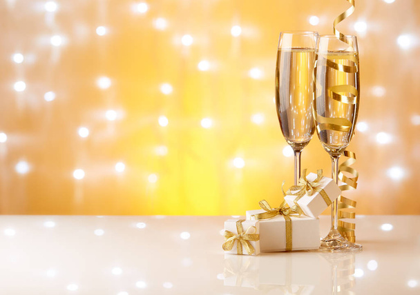 Two glasses with champange, gift boxes and christmas decorations on a yellow background with lights of garland.  New year and Christmas. - Foto, immagini