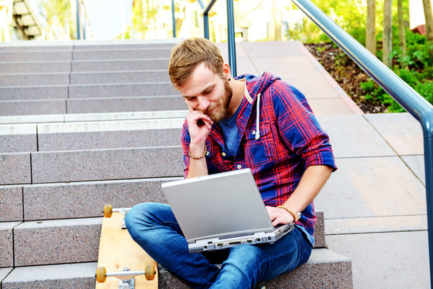 young man in checkered shirt sitting on stairs and using laptop - Φωτογραφία, εικόνα