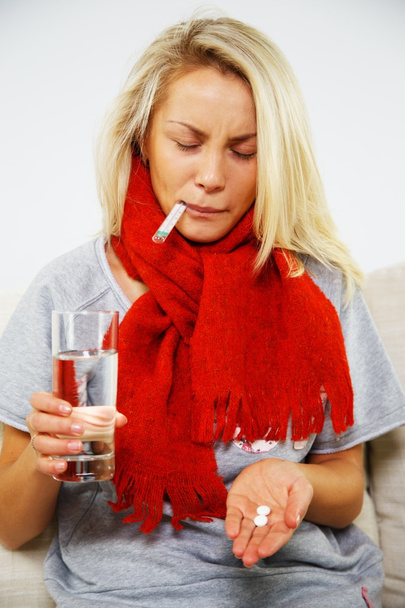Mujer rubia joven enferma con pastillas, termómetro y vaso de agua
 - Foto, imagen