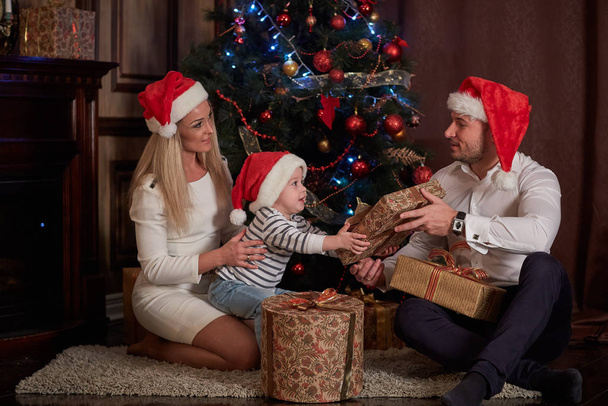 Happy family with  gifts sitting near Christmas tree at home. Merry Christmas and Happy New Year. - Foto, imagen